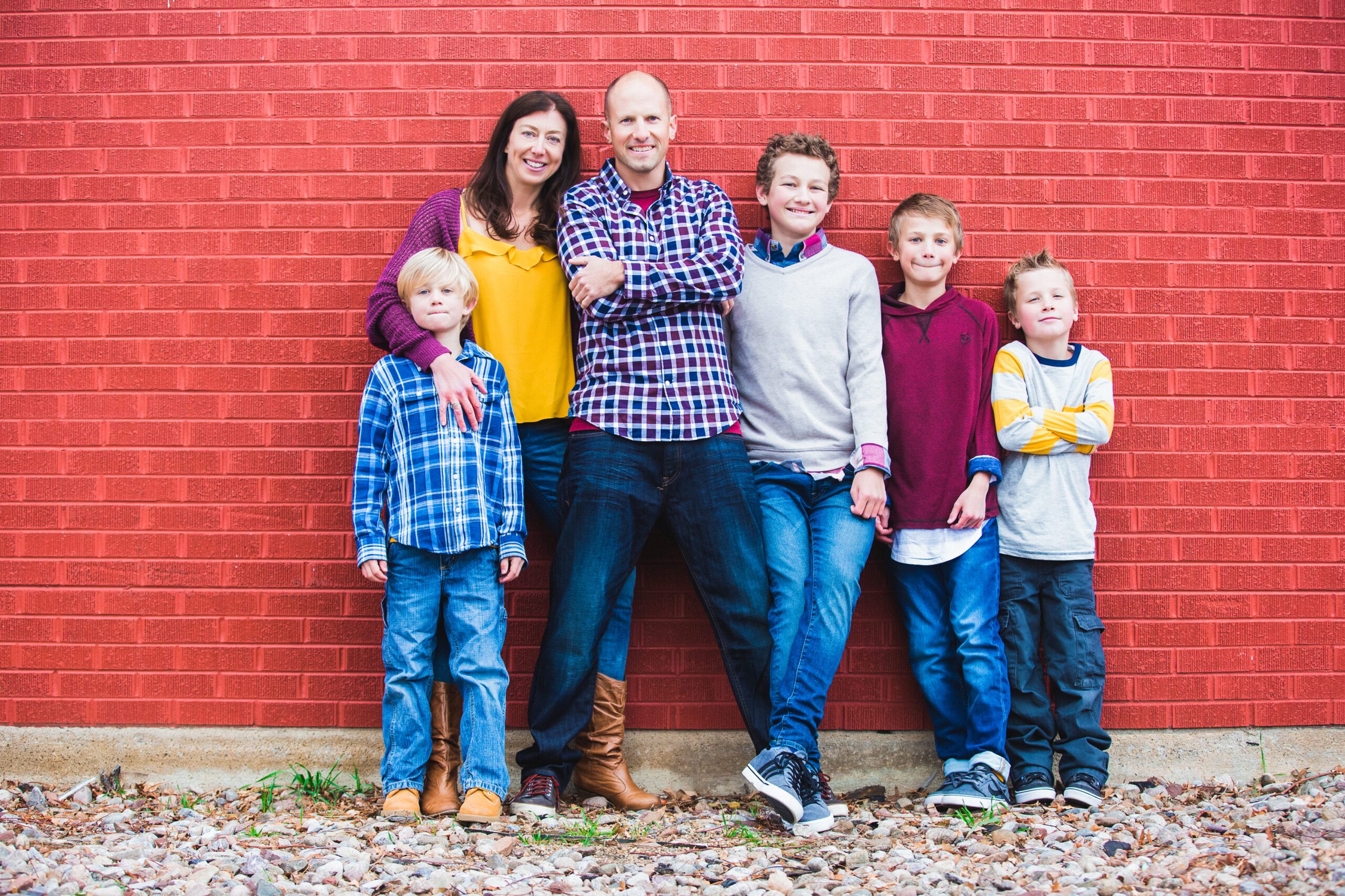 A happy family of six posing against a red brick wall.