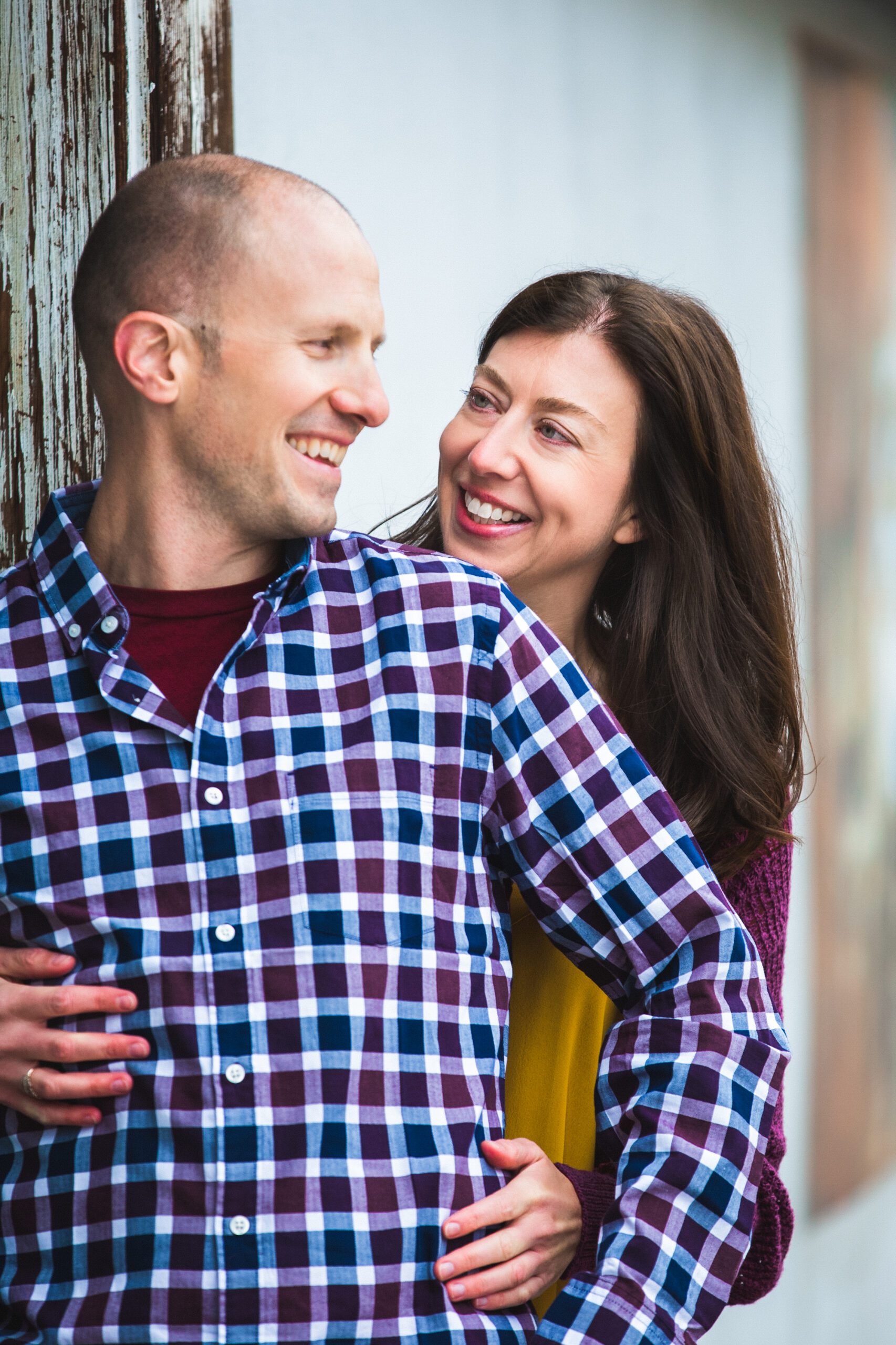 A smiling couple embracing next to a rustic backdrop