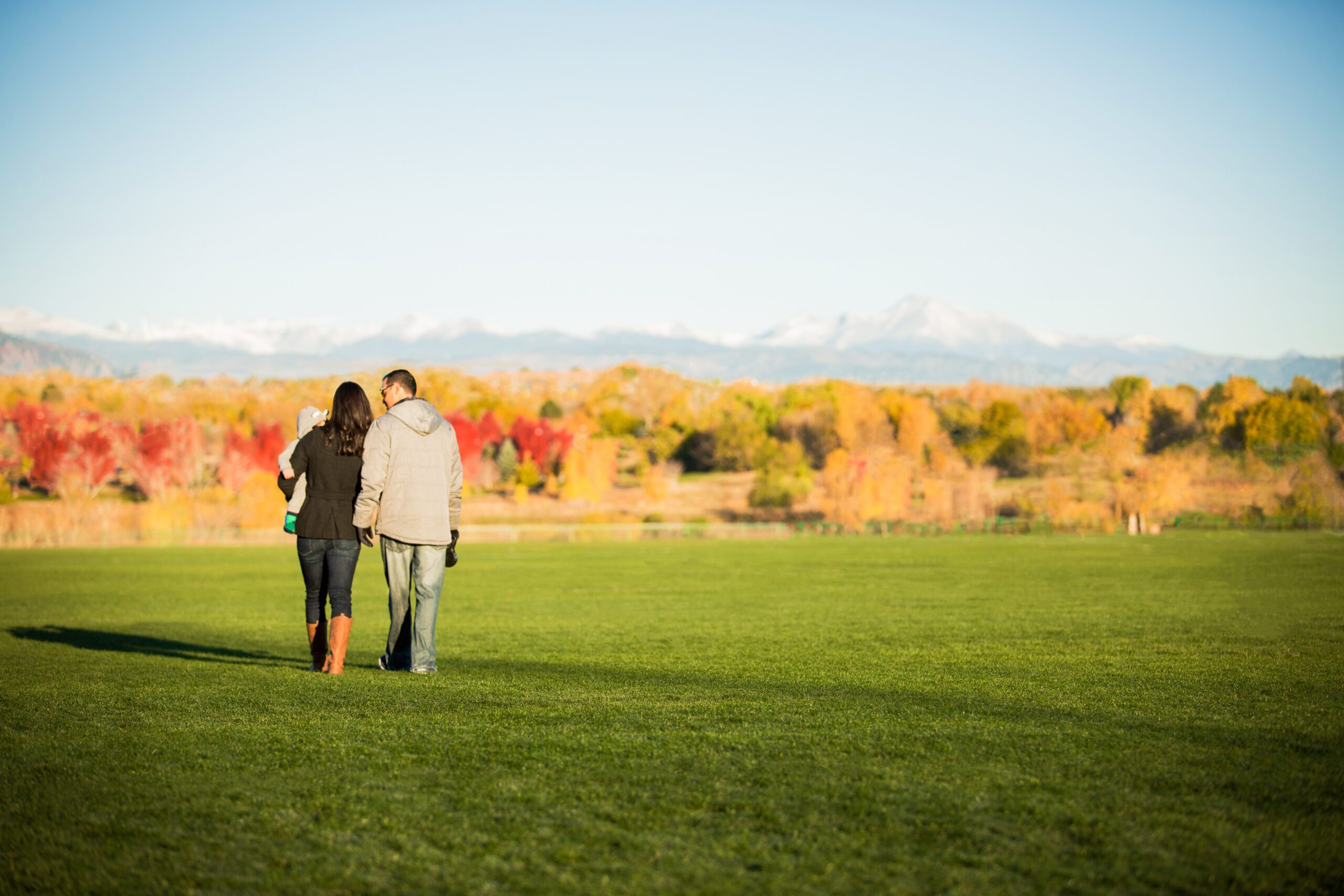 A couple with a toddler walking in a field with a mountainous backdrop