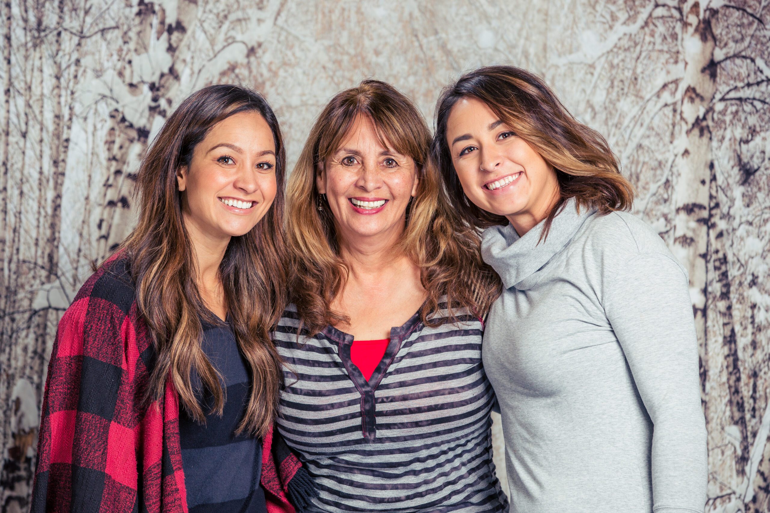 Three smiling women standing together in front of a patterned backdrop