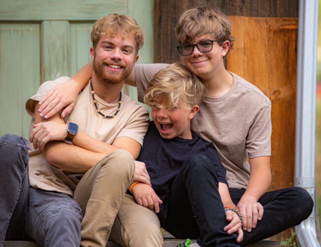 Three brothers sharing a joyful moment outdoors.