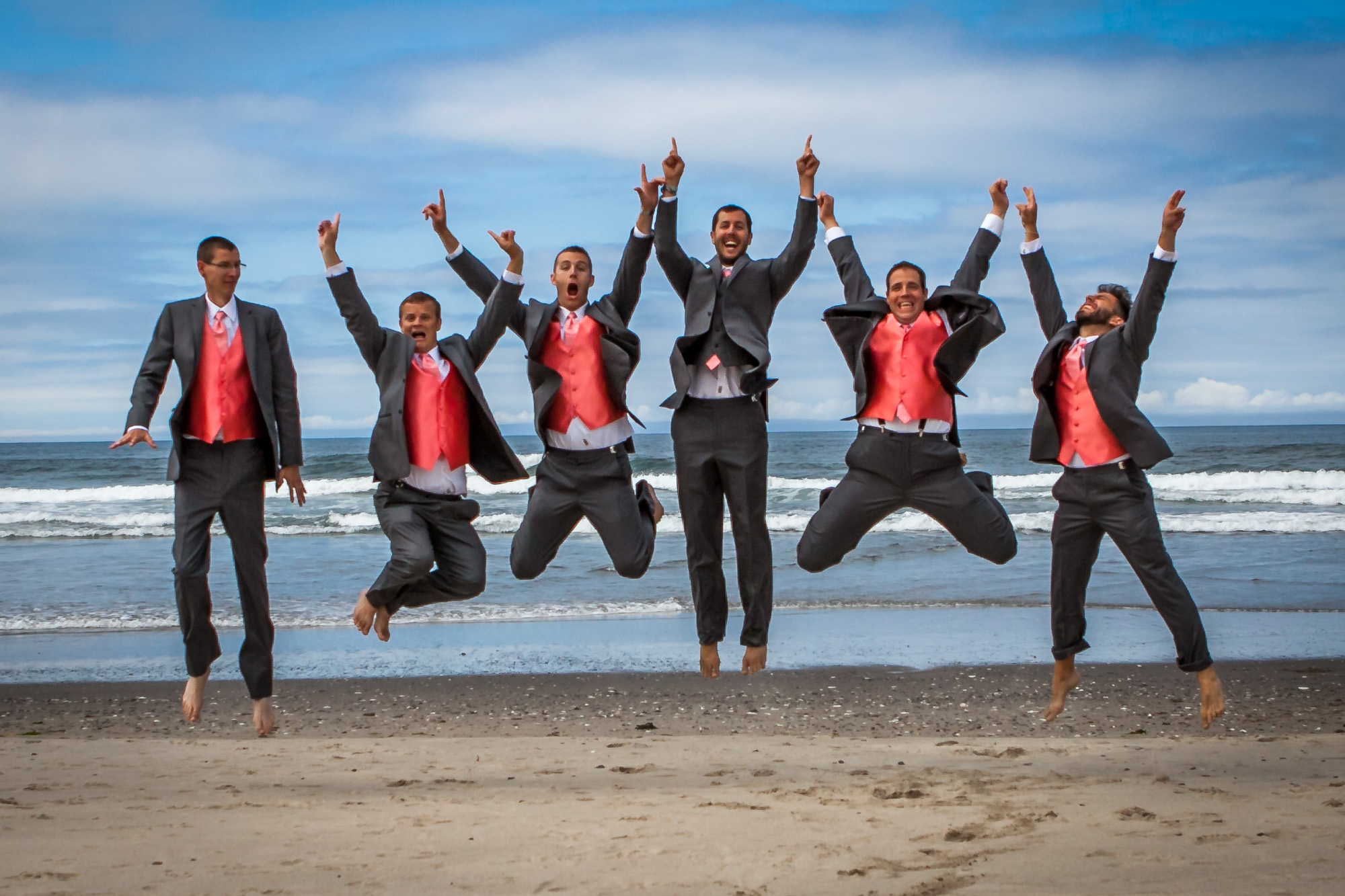 Exuberant groomsmen jumping on the beach in coordinated suits with red accents