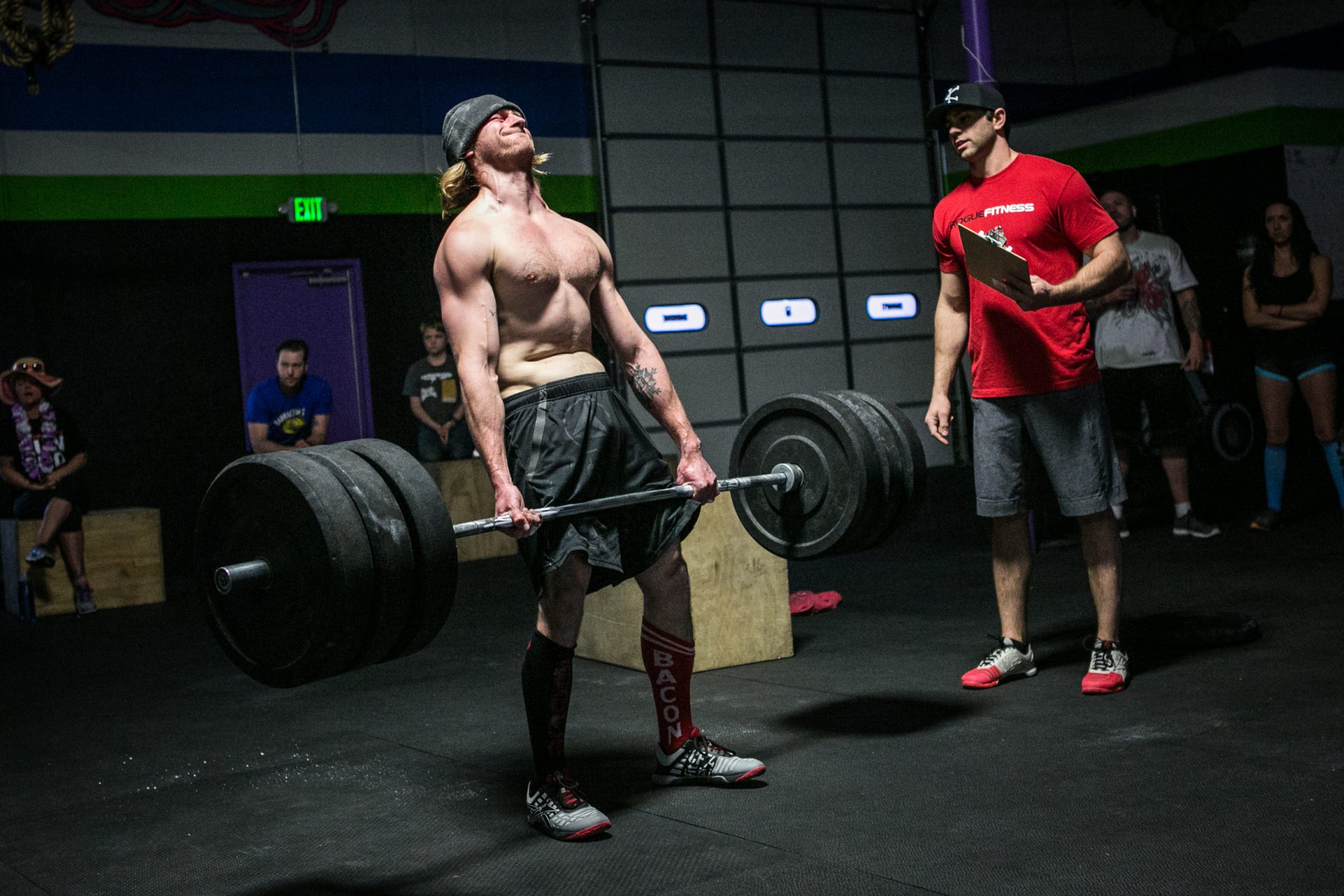 Male Athlete Deadlifting in Gym, Showing Strength With Coach and Spectators