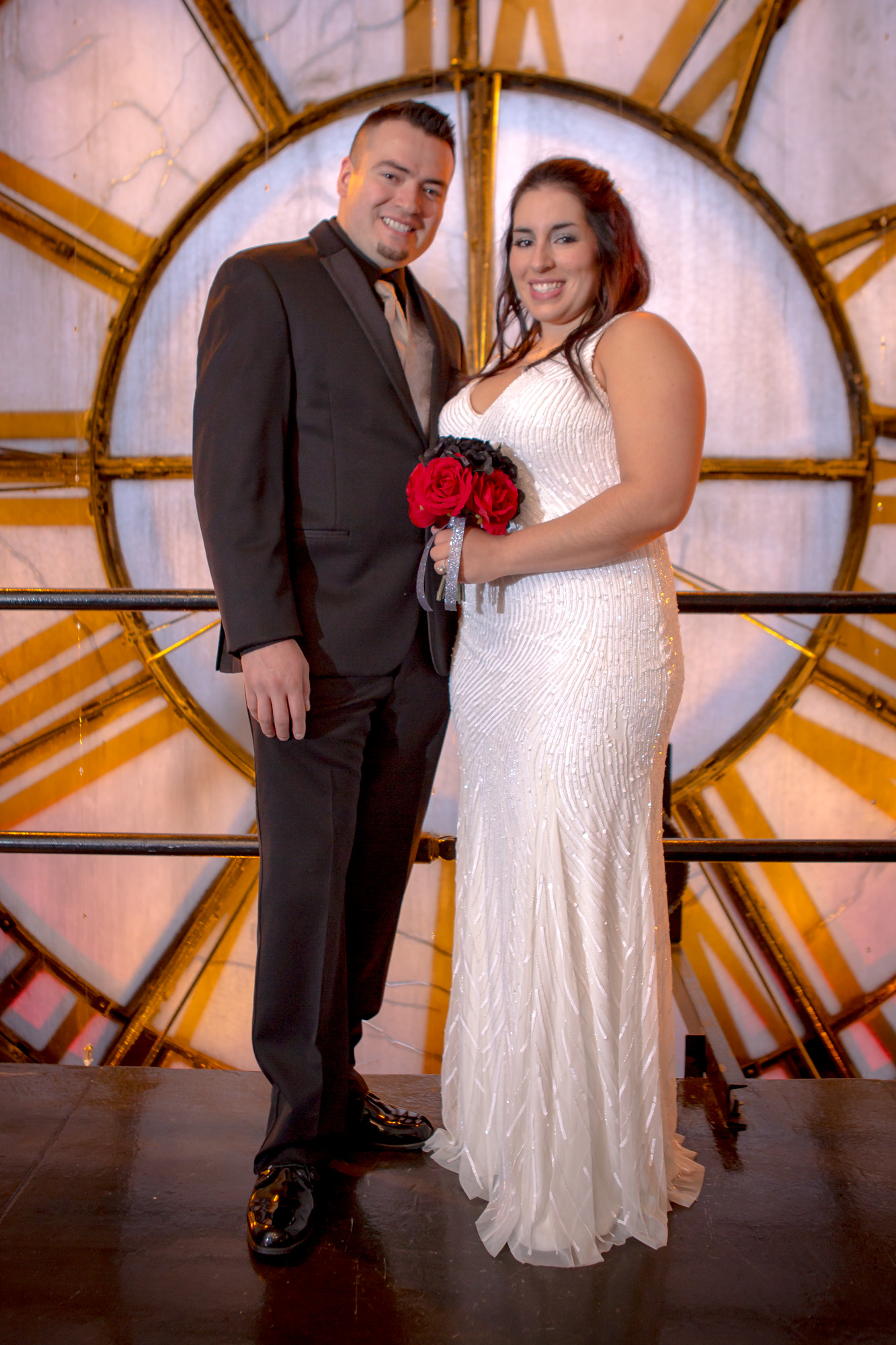 Happy couple in wedding attire, bride with red rose bouquet, in front of a grand circular window