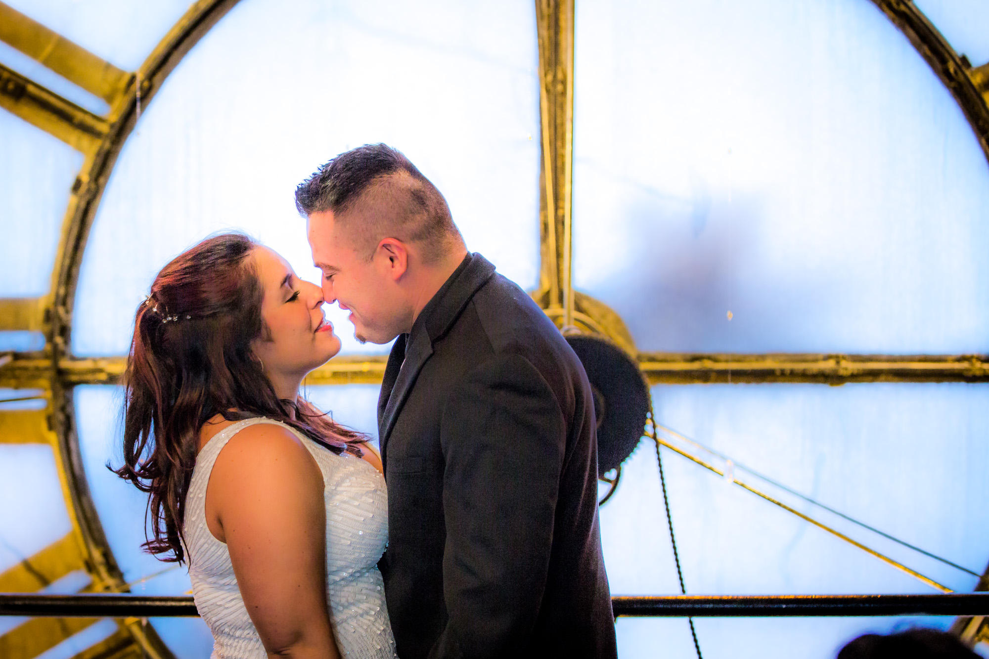 Bride and Groom Sharing a Close and Affectionate Moment in Front of a Large Circular Window With Soft Backlighting.