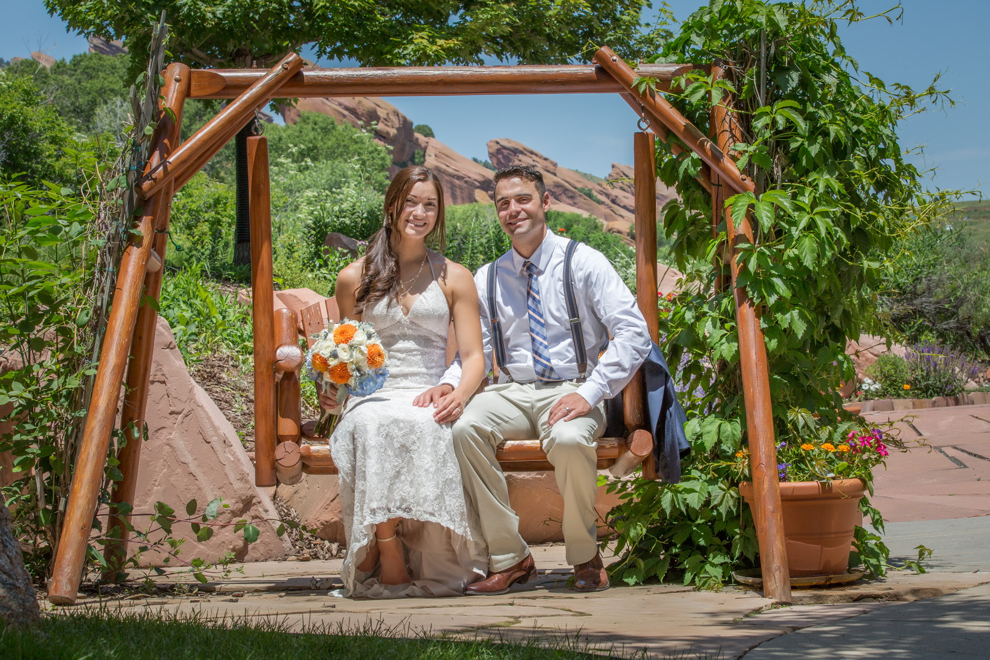 Newlywed Couple Sitting Under a Wooden Arbor With Red Rock Scenery in the Background, Celebrating Their Wedding Day