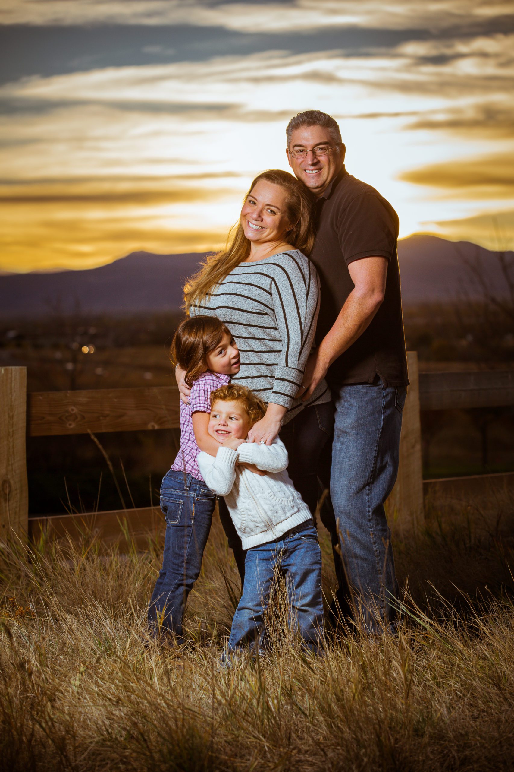 Family with two children embracing in a field at sunset