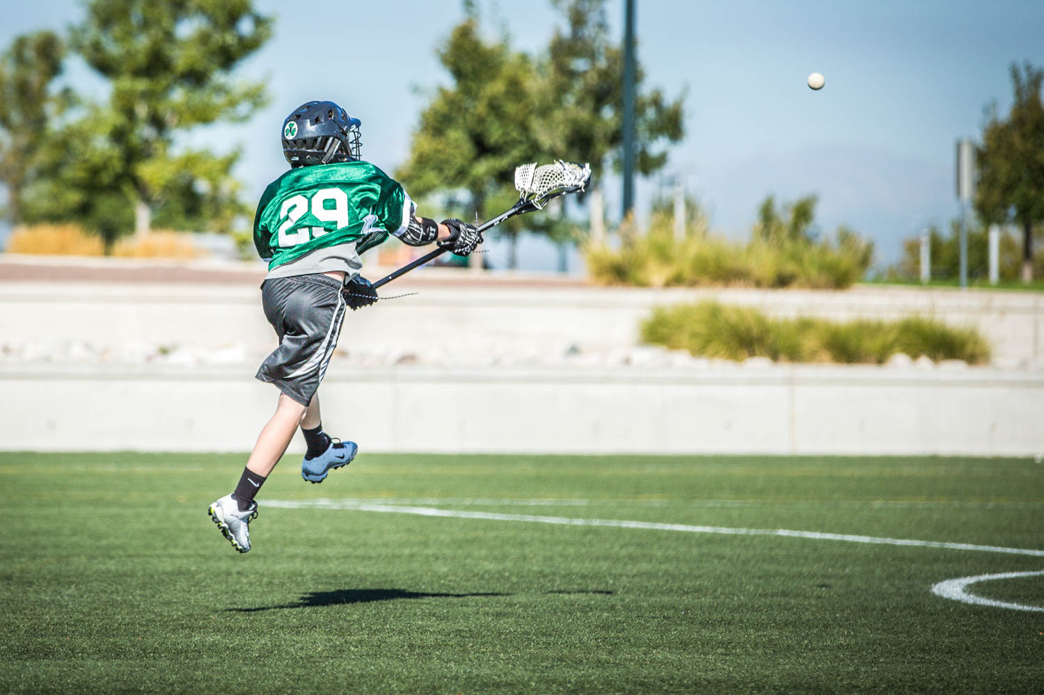 Young Lacrosse Player Number 29 in Action on Field with Blue Sky