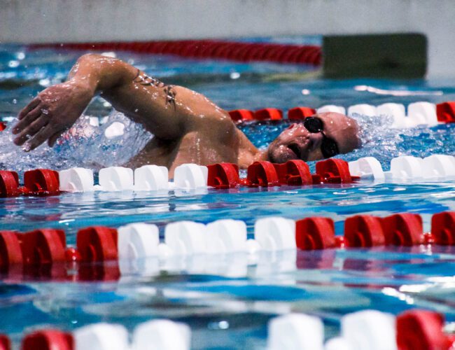 Swimmer Racing in Freestyle Event in Indoor Pool With Clear Water Splashes.