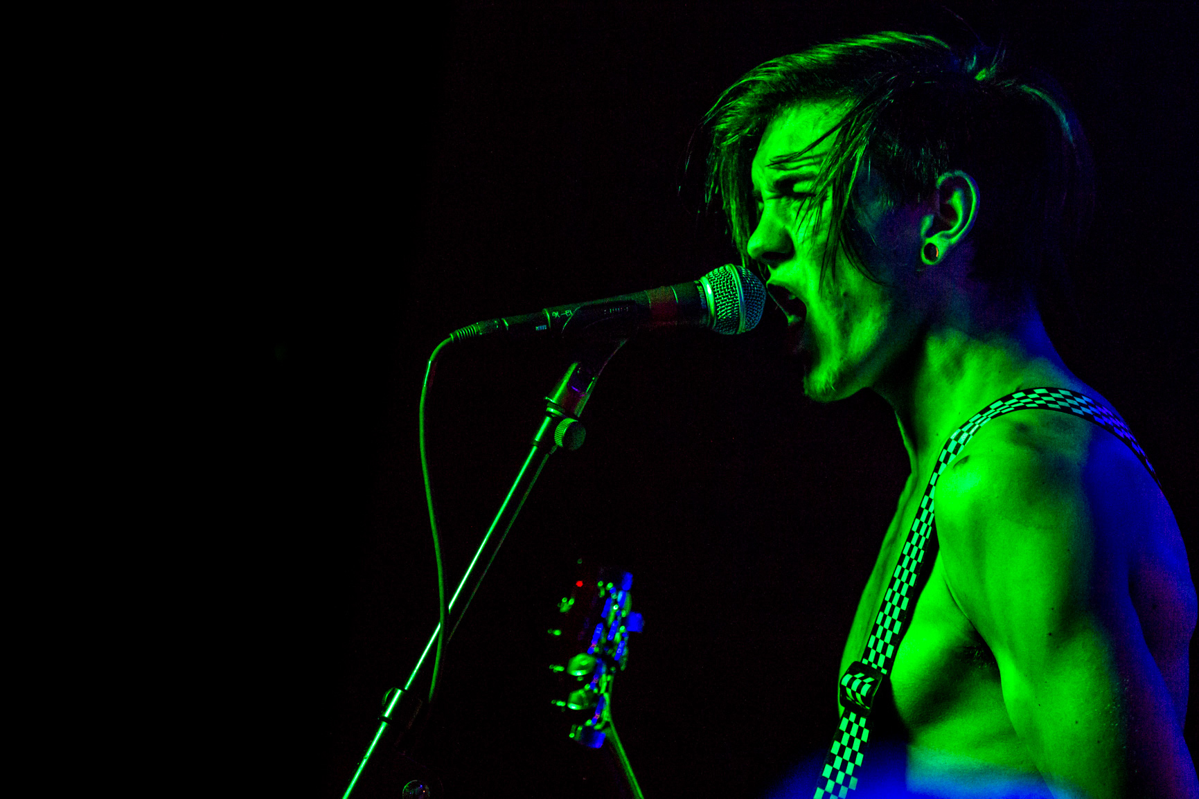 A singer and his guitar are glowing green from stage lighting at concert.