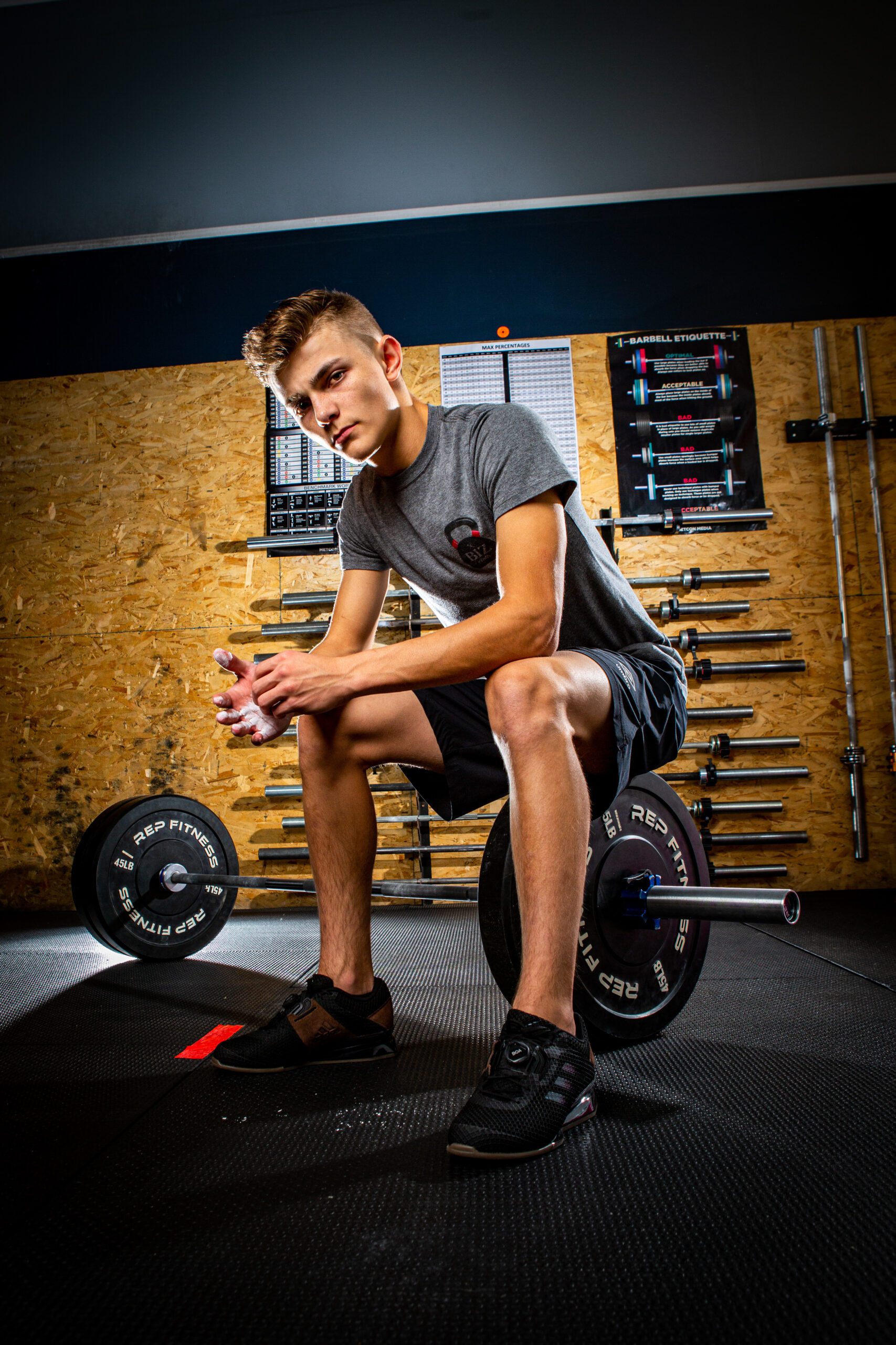 Determined senior man squatting next to a barbell in a gym with rows of barbells on the wall behind him