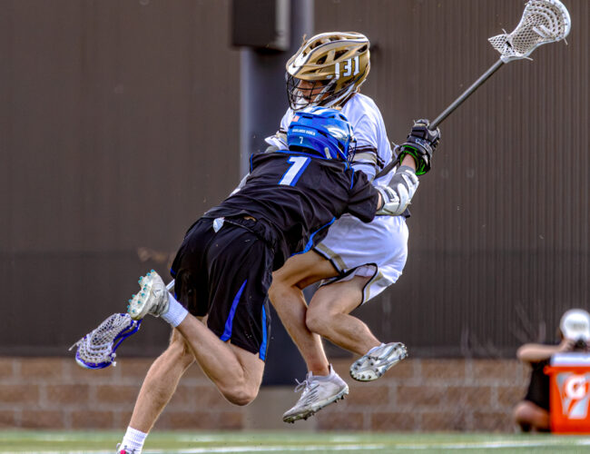 Highlands Ranch High School lacrosse defense player aggressively pushing aside an opposing team member during gameplay.