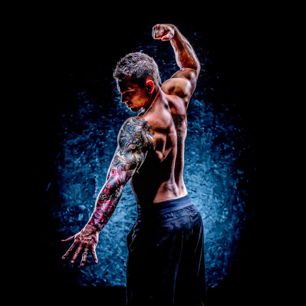 Tattooed male flexes his muscles in a classic bodybuilding pose.