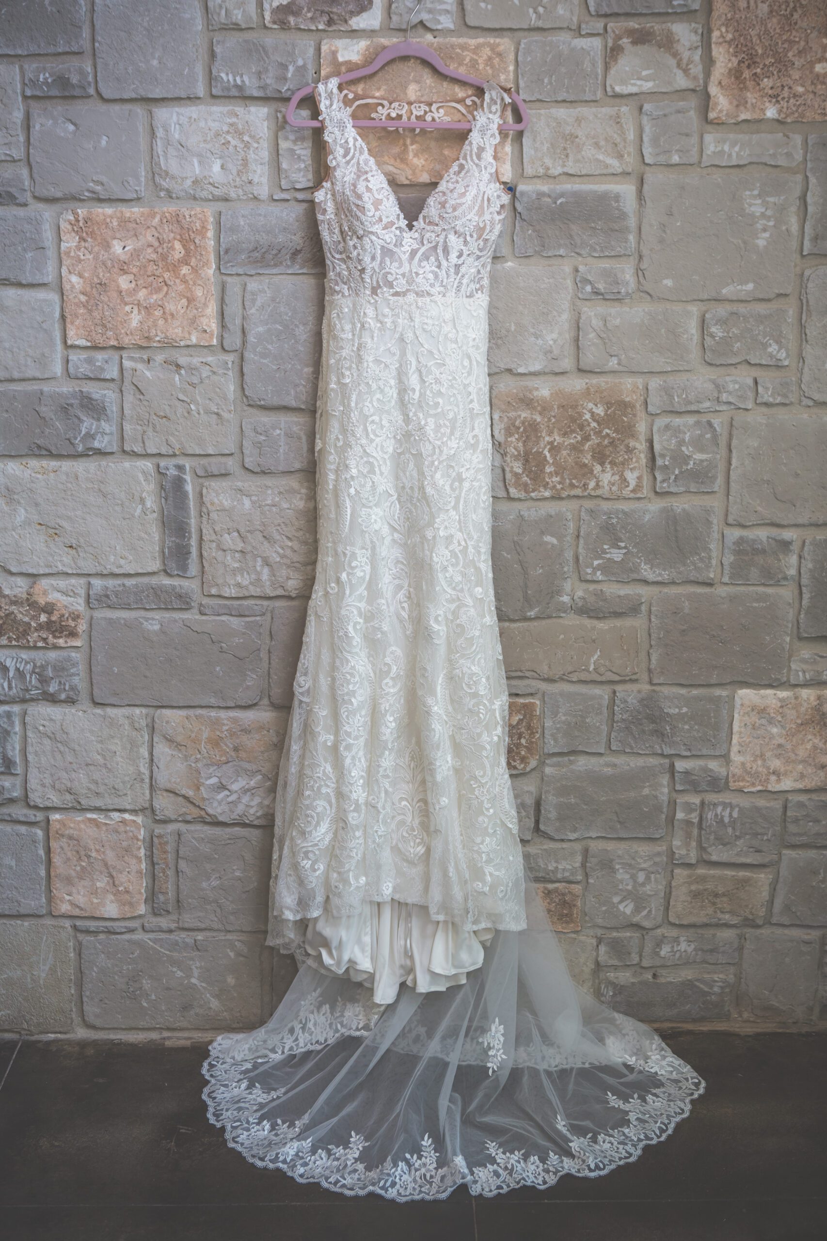 Elegant lace bridal gown with train and veil hanging against a stone wall